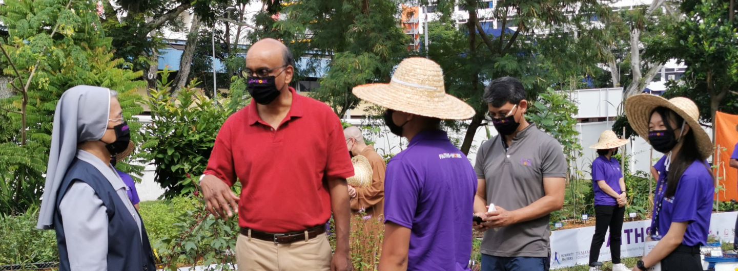 Group in outdoor garden, some wearing masks and sun hats, "Faith-Works" T-shirts visible.